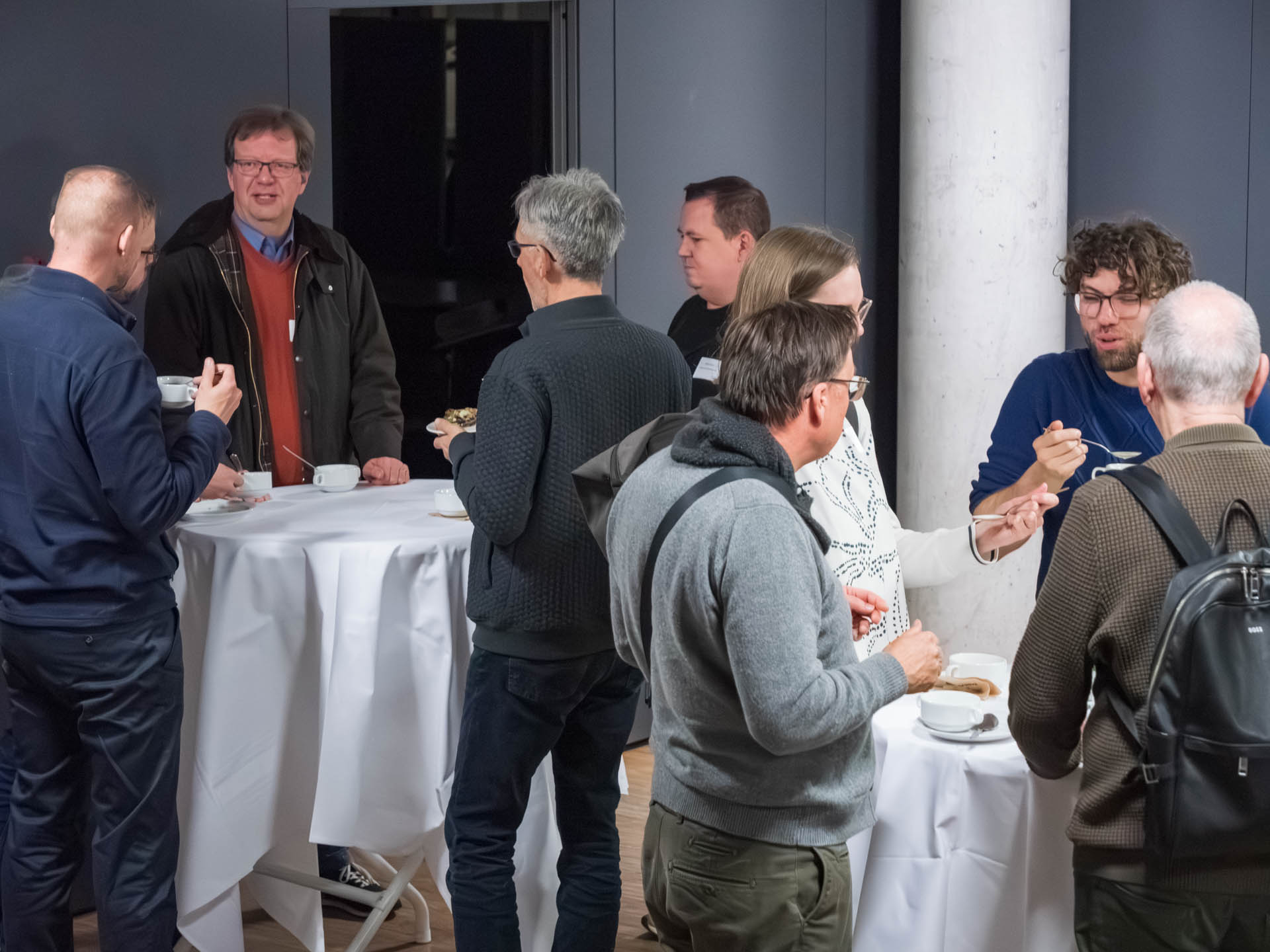 Mehrere Personen essen und sprechen an Stehtischen 